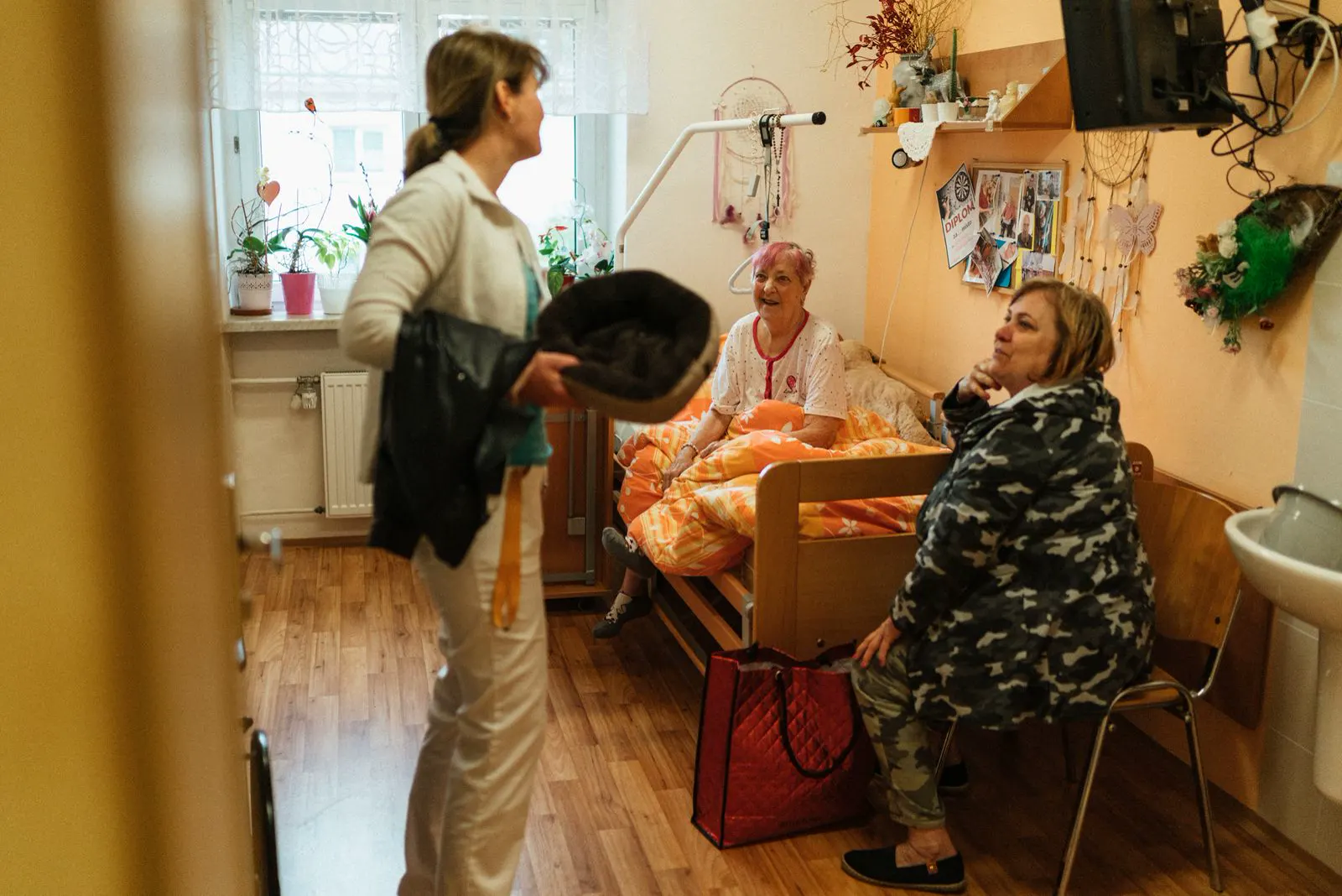 A caregiver talks with two older women in a care-home living room.