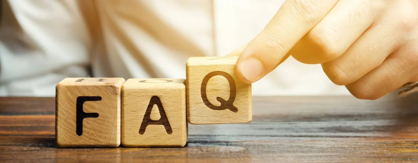 Une personne tient un bloc de bois sur lequel le mot FAQ est écrit.