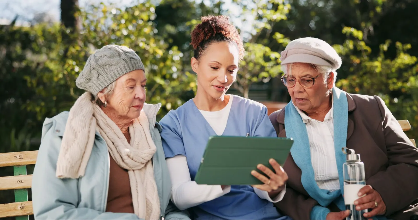 Un membre du personnel infirmier montre à deux femmes aînées comment utiliser une tablette.
